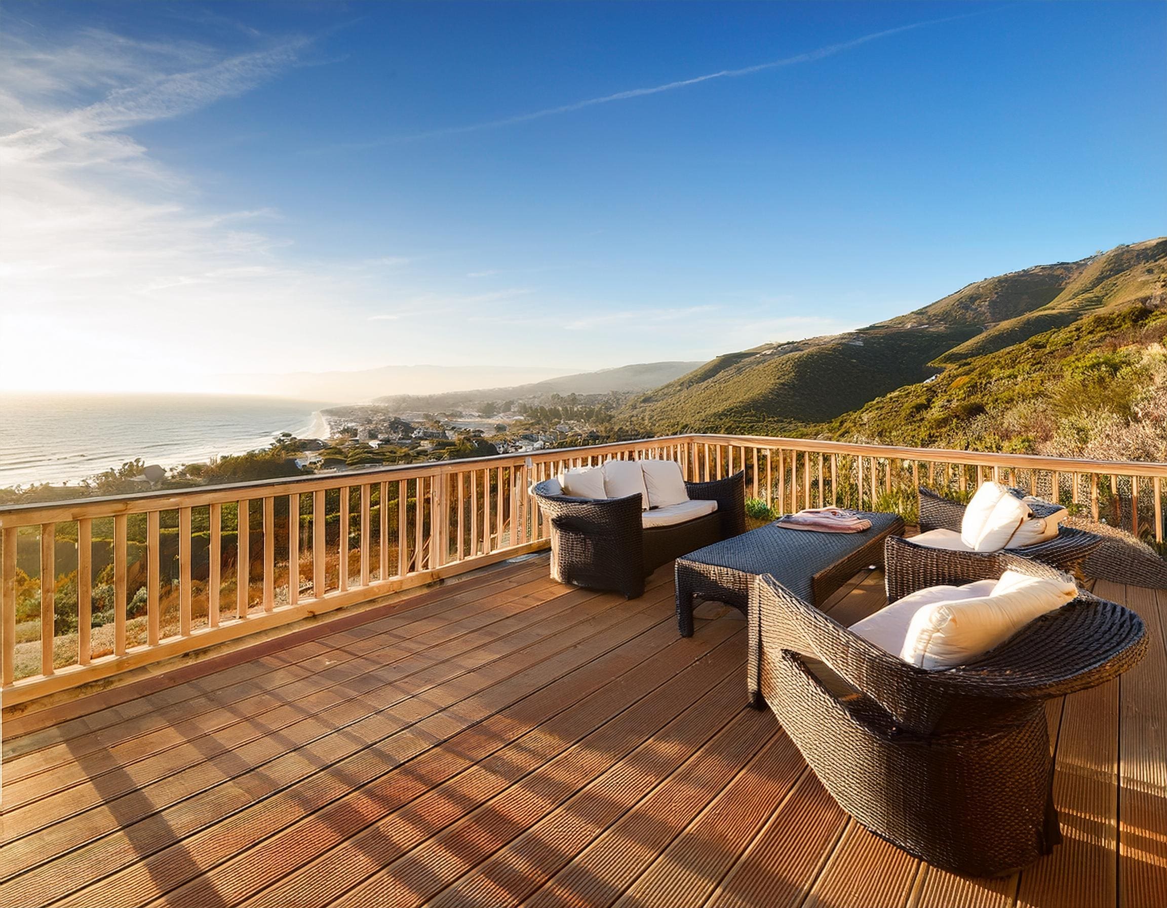 A spacious wooden deck furnished with outdoor seating, overlooking a coastal California landscape. J Kidd Construction